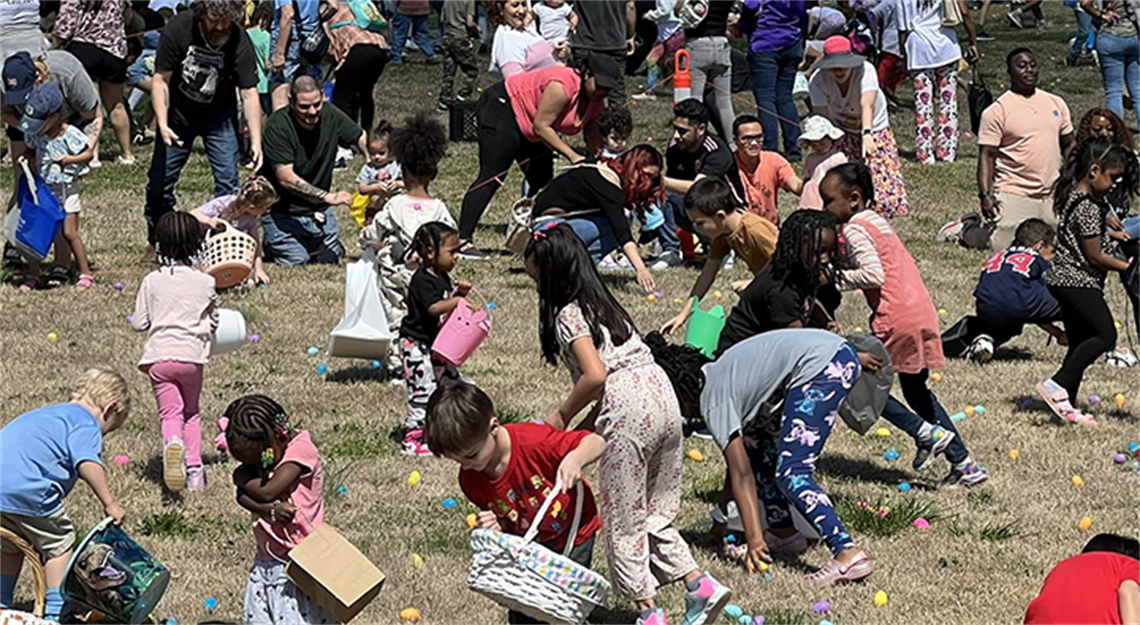 Large crowd of kids hunting Easter eggs as adults watch